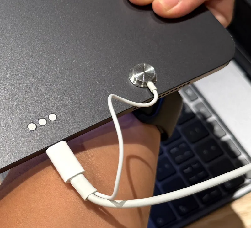 Style reference photo taken at an Apple Store: hand lifting a device with a round contact sensor and slim cable on its back (not a Tocvue product)