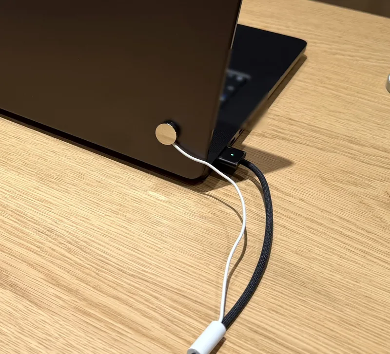 Style reference photo taken at an Apple Store: laptop lid back with a round contact sensor and charging cable in the side port (not a Tocvue product)