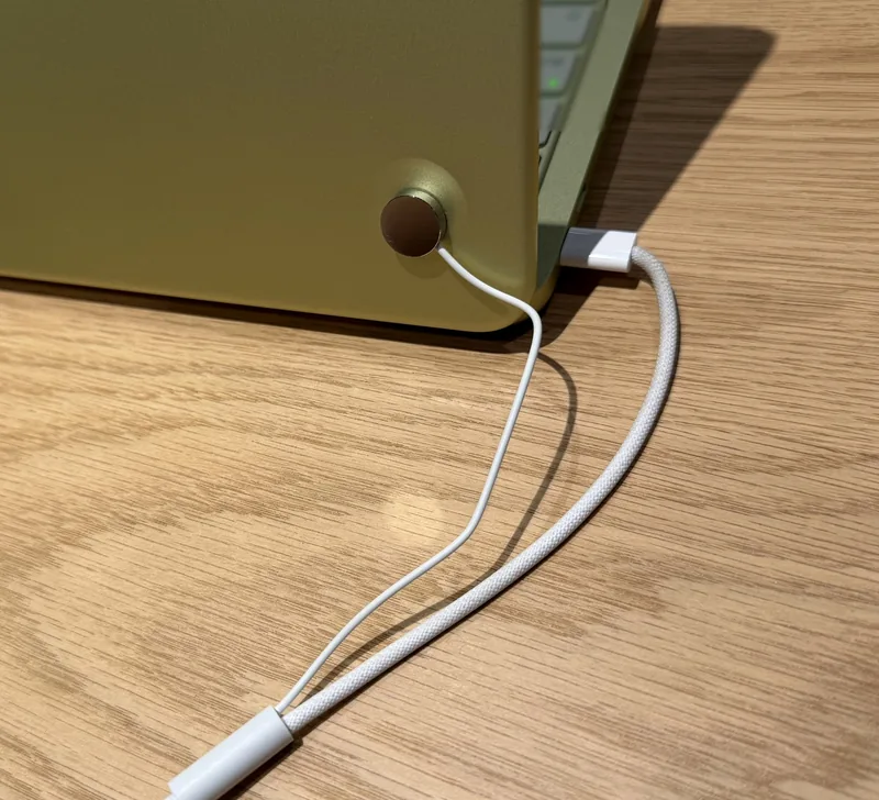 Style reference photo taken at an Apple Store: round contact sensor and USB-C charging cable on a laptop lid back (not a Tocvue product)